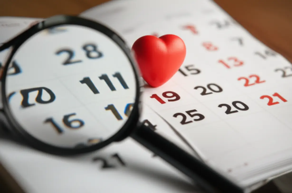 큰-달력-페이지-뒤에-작은-하트-기호가-숨겨져-있고,-돋보기가-그것을-찾으려-하고-있다.